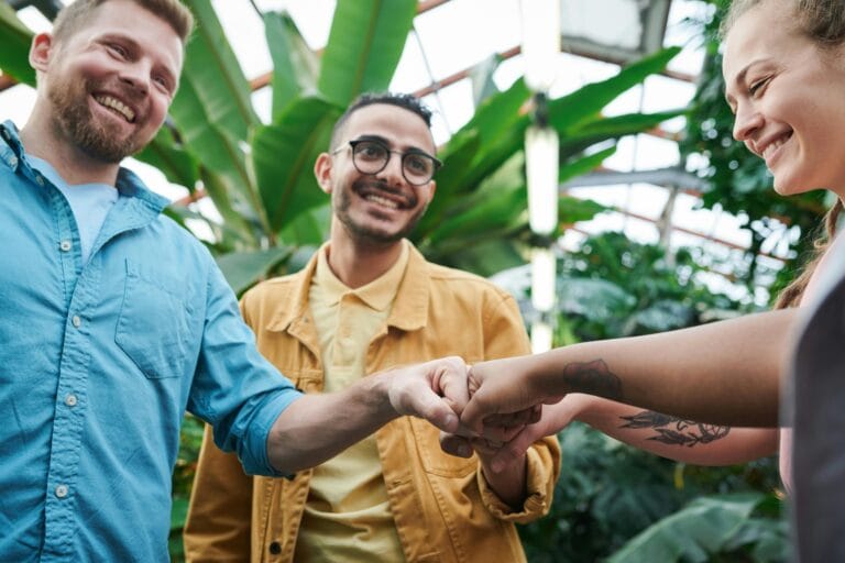 Three friends sharing a joyful fist bump in a lush indoor greenhouse environment.