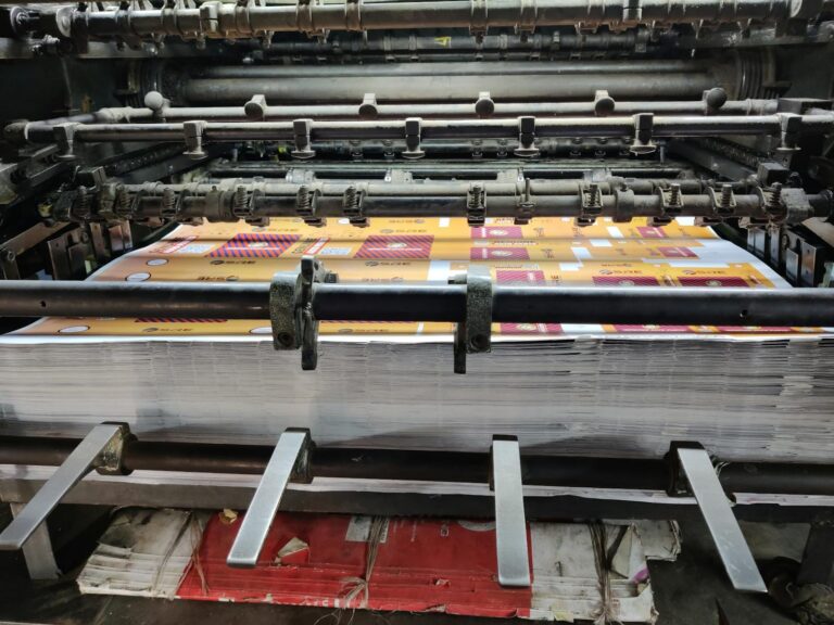 Primer plano de una máquina de impresión industrial procesando hojas de papel en una fábrica.
